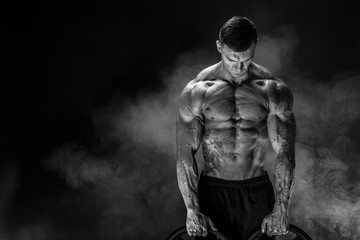 Fototapeta na wymiar Very brawny guy bodybuilder. Bodybuilder with dumbbells in his arms on dark background with smoke.