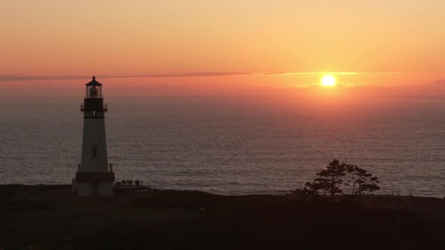 Georgous shot of the Yaquina Head Lighthouse as the evening sun disappears in the purple horizon on the Pacific Ocean along the Oregon Coast