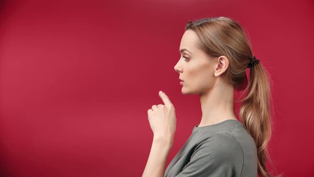 Half-face of adorable young blonde girl showing gesturing shushing isolated at red studio background