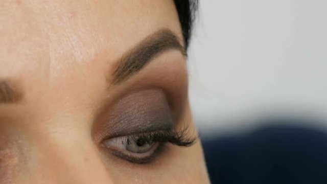 Beautiful blue eye to a young woman whom apply smoky eyes with the help of special brush Lilac and pearly smoky eyes eyeshadow, eyes and face of woman close up view. Professional high fashion.