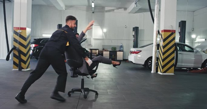 Auto service center the office worker lady and mechanic guy have a fun time they drive on a chair and going crazy while have a break time