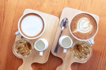 A cup of coffee, cappuccino and latte, complete with syrup and tea on a wooden plate