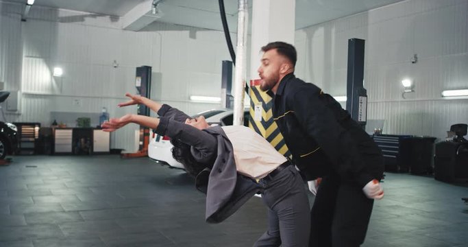 In A Large Service Auto Center Happy And Excited Manager Woman In A Suit And Mechanic Guy In A Uniform Dancing In Front Of The Camera