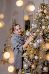 Beautiful girl decorating Christmas tree. a young smiling woman prepares a Christmas tree for the holiday. Lush green Christmas tree with Golden balls