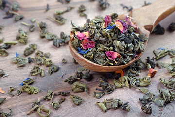 blended tea. green tea with dry flower petals. dry green tea leaves in a wooden spoon. close up