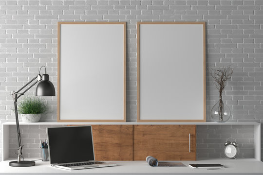 Workspace with two vertical poster mock ups on the desk. Desk with drawers in interior of the studio or at home with white brick wall. Clipping path around poster. 3d illustration.