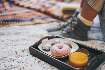 Young woman lying on colorful bed having breakfast on holidays. Morning in a cozy warm bedroom with natural juice Christmas cookies and and donut. Happy young girl thinking on wishes for the new year