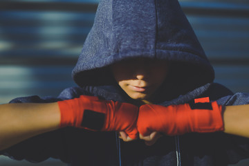 Young male hands with boxing bands ahead the face. Boy prepares for a boxe workout by wrapping his hand. Boxer ready to throw punches. Teenager Sport, youth, determination and training gym concept.