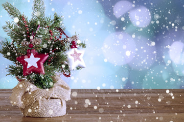 little christmas tree decorated with stars in winter environment over wooden table with christmas lights and snow in the background