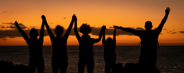 Silhouette of a family hand in hand enjoying a beautiful sunset at the beach. Group of friends...