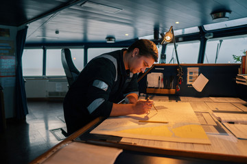 Marine navigational officer during navigational watch on Bridge . He does chart correction of...