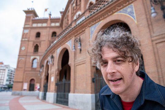 A man travels in Madrid, Spain, visiting the Las Ventas bull fighting ring, and takes a photo in the plaza outside.