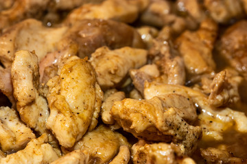 Marinated torn cut chicken bits being cooked, halfway cooked. Spicy chicken, wooden spatula