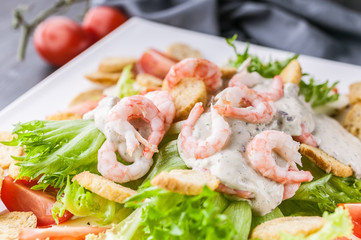 Close-up appetizing salad with shrimp, lettuce, cheese, avocado and crackers on a white plate. Delicious and healthy seafood recipes. Low calories