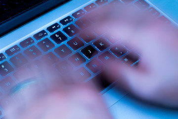 A Person typing really fast at on a laptop at night 