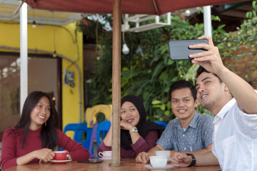 Multiracial group of four asian friends having a coffee together. Two women and two men at cafe, talking, laughing and enjoying their time