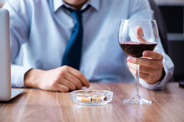 Male employee drinking alcohol and smoking cigarettes at workpla