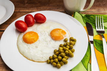 Two fried eggs with a green pot and tomatoes for a healthy breakfast.