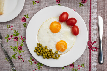 Two fried eggs with a green pot and tomatoes for a healthy breakfast.