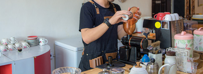 Handsome Asian barista pouring coffee bead into grinder machine