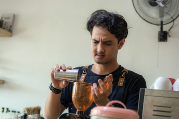 Handsome Asian barista pouring coffee bead into grinder machine