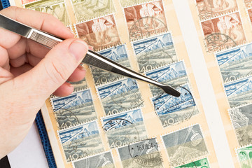 Fototapeta na wymiar SEATTLE, WASHINGTON - MAY 29, 2019: Hand holding tongs insets, or removes, used duplicate postage stamp into a stock book