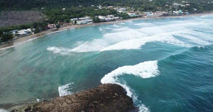 Aerial shot of Jobos Beach rock with waves crashing and town in background