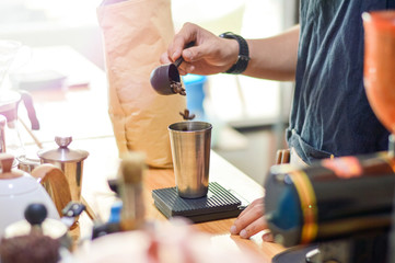 Close up of barista hand pouring coffee bean to the stainless glass