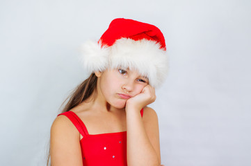 little cute girl is standing in a Christmas hat is sad