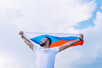 young guy in a white T-shirt with a stretched Russian flag against a blue sky on a hot day, fans...