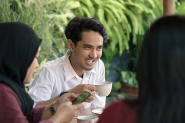 Asian handsome man enjoying coffee or tea with his girlfriend sitting in an outdoors cafe.