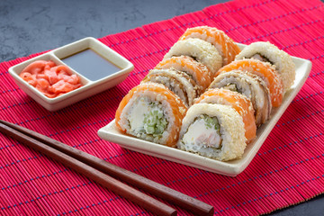 Sushi roll, chopsticks, soy sauce, ginger and red bamboo mat.