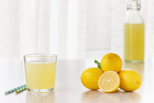 A glass of lemon juice and lemons around on a table.