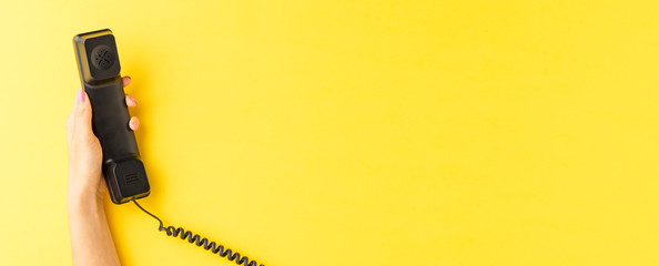 Female hand holding vintage phone on yellow background. Call center concept. Banner