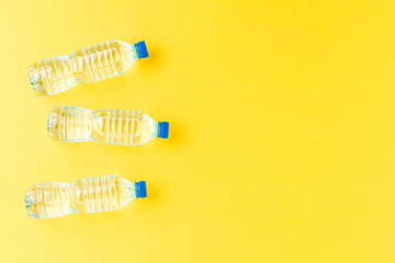Mineral water in small plastic bottles on yellow background with copyspace. Top view