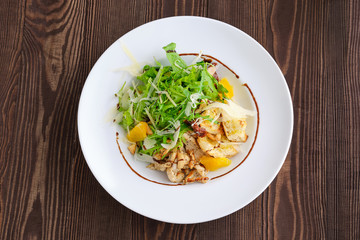 Top view of salad with fried chicken meat, dried tomato, cashew nuts and orange balsamic sauce served with arugula and parmesan on dark wooden background