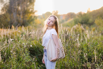 girl with long hair in field at sunset, linen bag