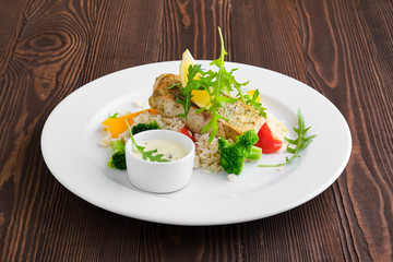 Fried zander with rice, bell pepper and arugula served with mayonnaise sauce on dark wooden background