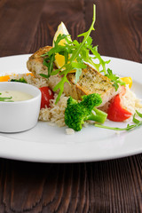 Soft focus photo of fried zander with rice, bell pepper and arugula served with mayonnaise sauce on dark wooden background