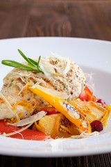 Closeup view of fried turkey meat with roasted tomato and bell pepper served with parmesan, cranberry and orange balsamic sauce on dark wooden background