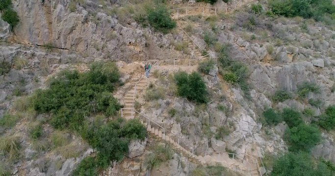 Senior descendiendo por escalera en pared de piedra vertical y un dron alej&aacute;ndose