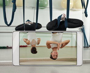 Young woman using hammock and practicing fly yoga, concept of new features of smart device. Original items have been removed from the front panel