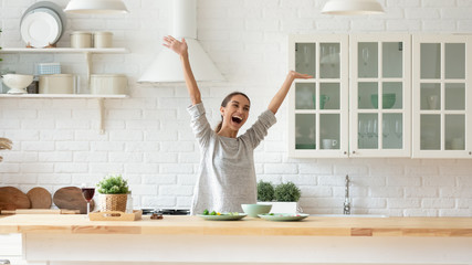 Overjoyed young woman raise hands feel excited cooking in kitchen