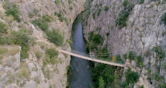 Anciano cruzando puente colgante entre paredes verticales de piedra