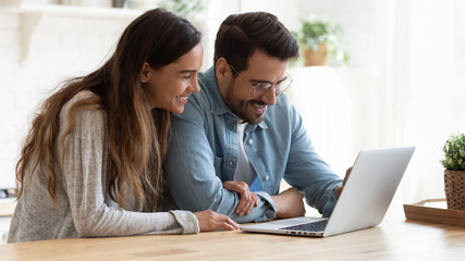 Happy young couple bonding laughing using laptop sit at table