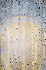 Drops of water flow down the surface of a transparent glass on an abstract blurred bright colored background.