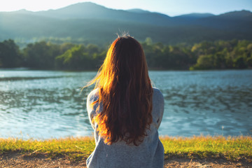 A woman sitting alone by the lake looking at the mountains with green nature background