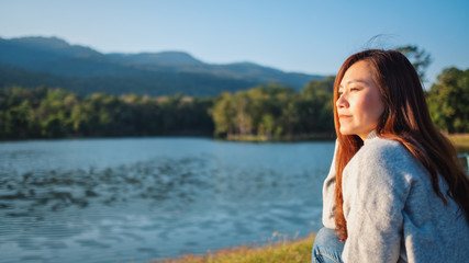 Portrait image of a beautiful asian woman sitting in front of the lake and mountains before sunset