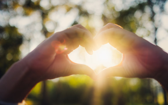 Closeup image of sunlight shining through heart hands sign with nature background