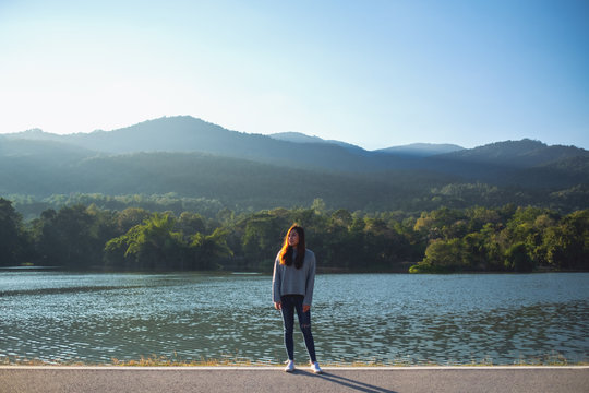 Portrait image of a beautiful asian woman standing alone in front of the lake and mountains on sunny day